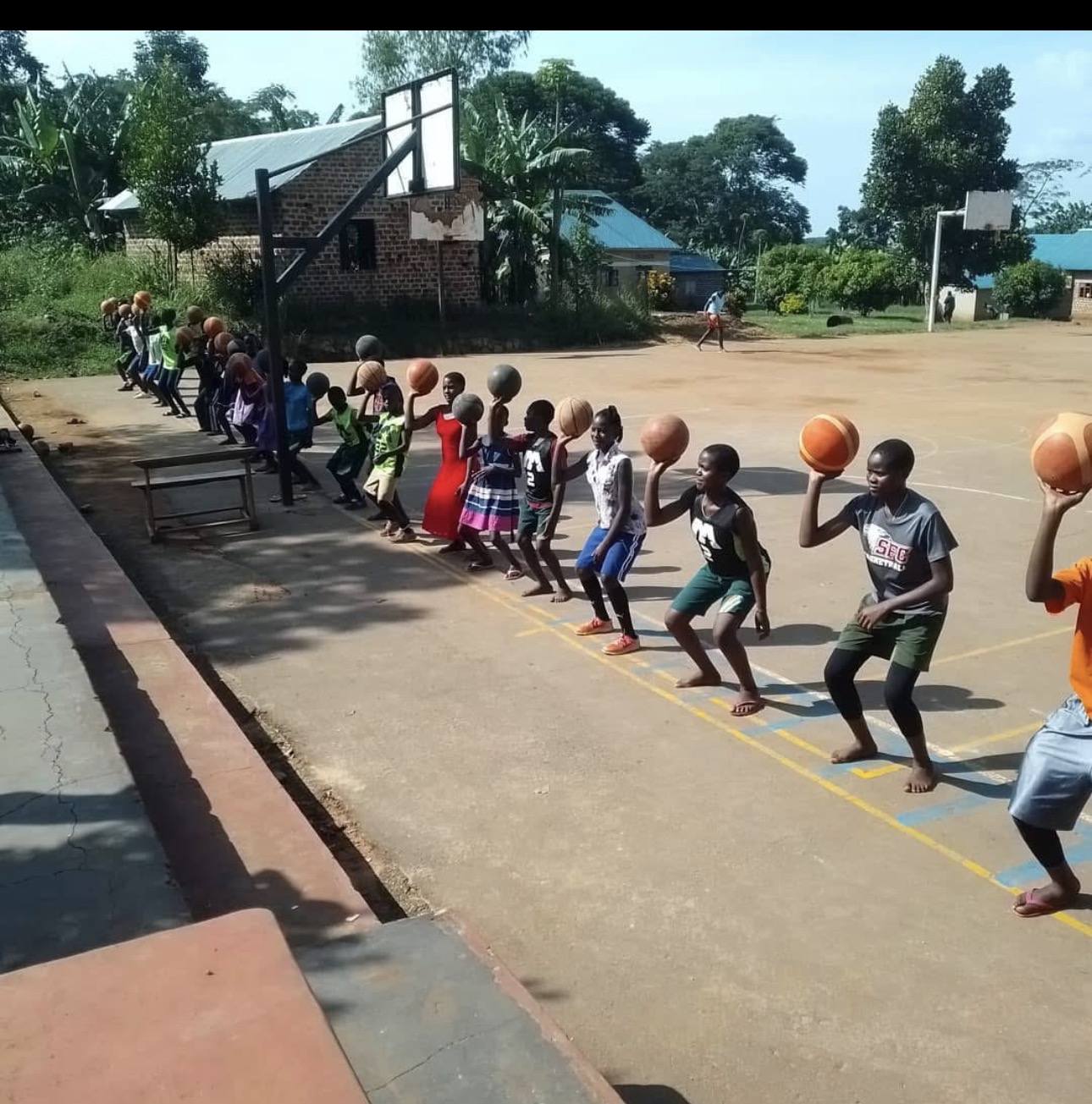 Children lined up holding basketballs on the court